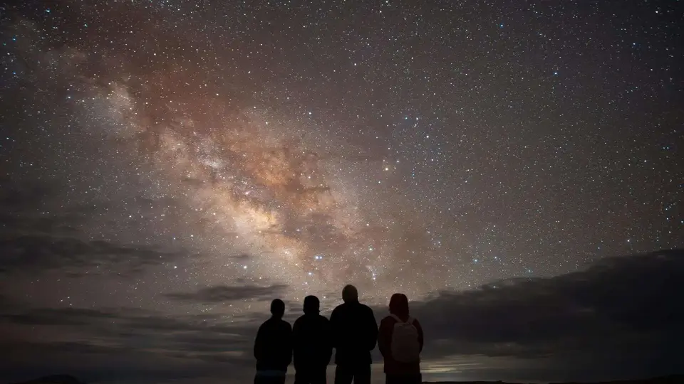 Four people silhouetted under a breathtaking night sky, gazing at the Milky Way in a remote location. A magical stargazing moment capturing nature and the cosmos.
