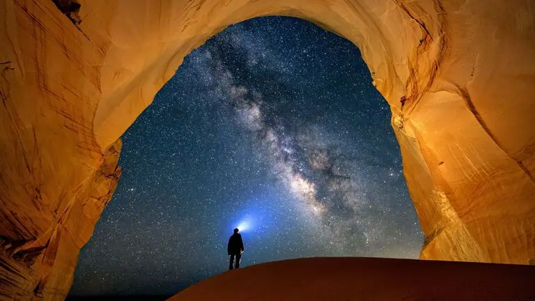 Stargazing under the Milky Way from a sandstone arch in a desert canyon. A breathtaking night sky scene perfect for astronomy lovers and adventure travelers.